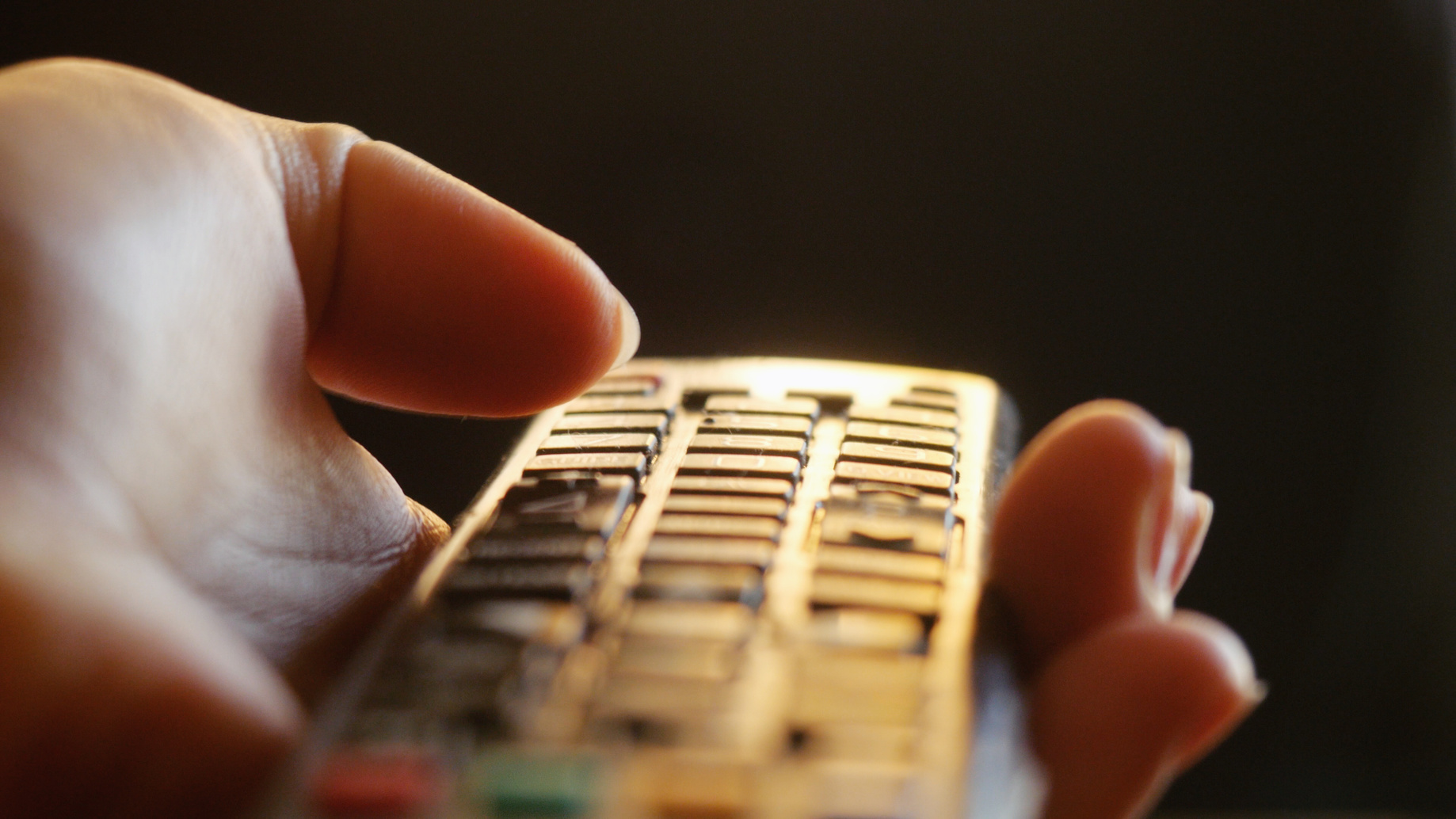 Close up of woman's hand with a television remote control changing channels at sunset time
